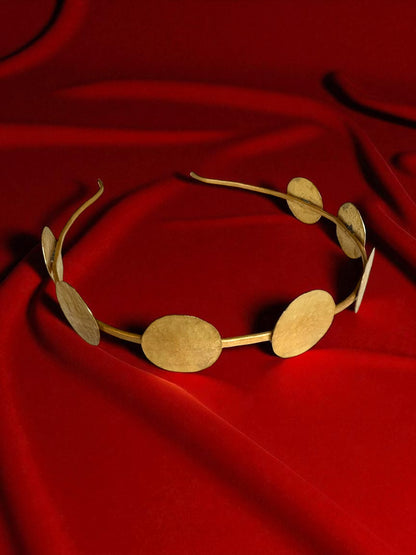 Gold headband with circular designs on a red fabric background